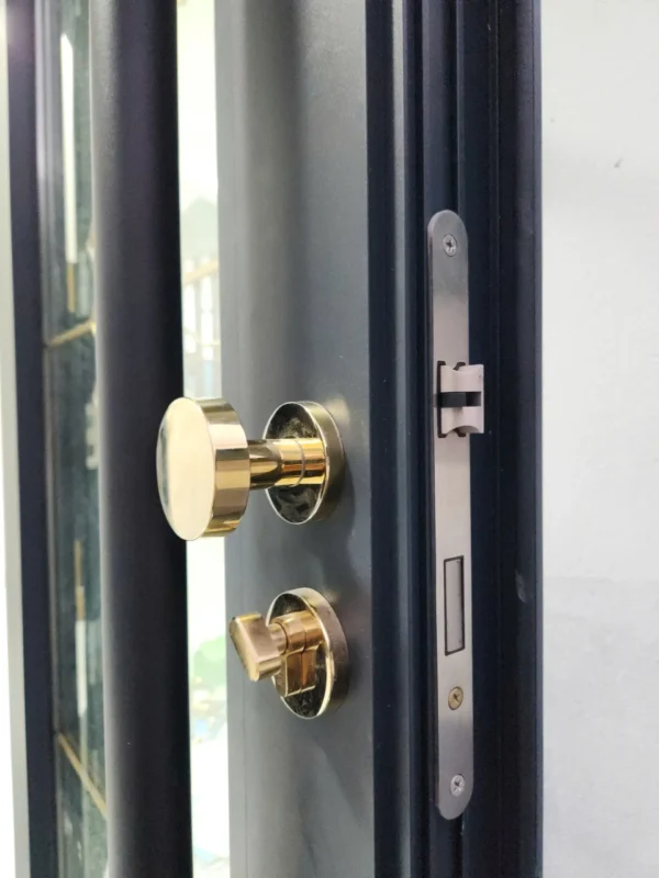 Cận cảnh tay nắm tròn màu vàng, nút vặn khóa và thân khóa âm trên cửa nhôm xám đen