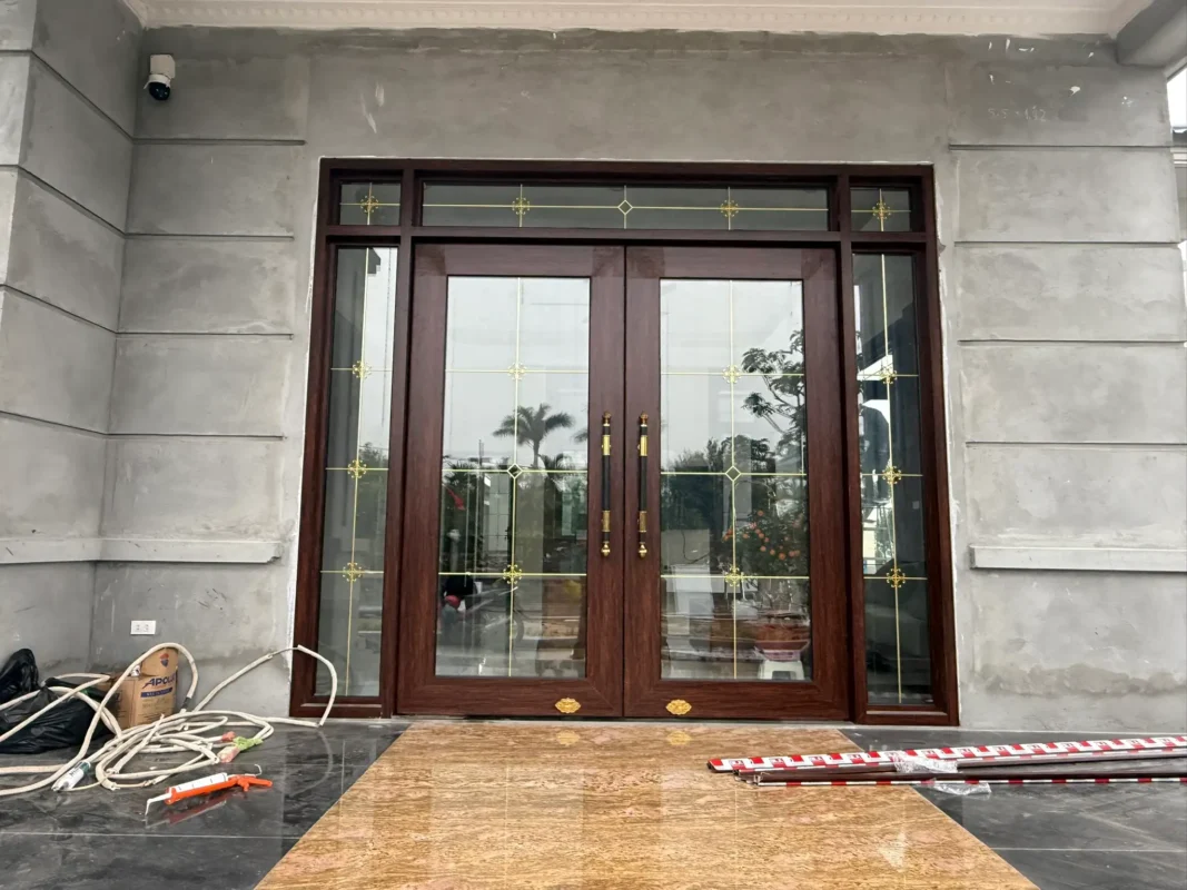 Cửa chính vân gỗ nâu lắp ở nhà đang hoàn thiện, tường chưa sơn