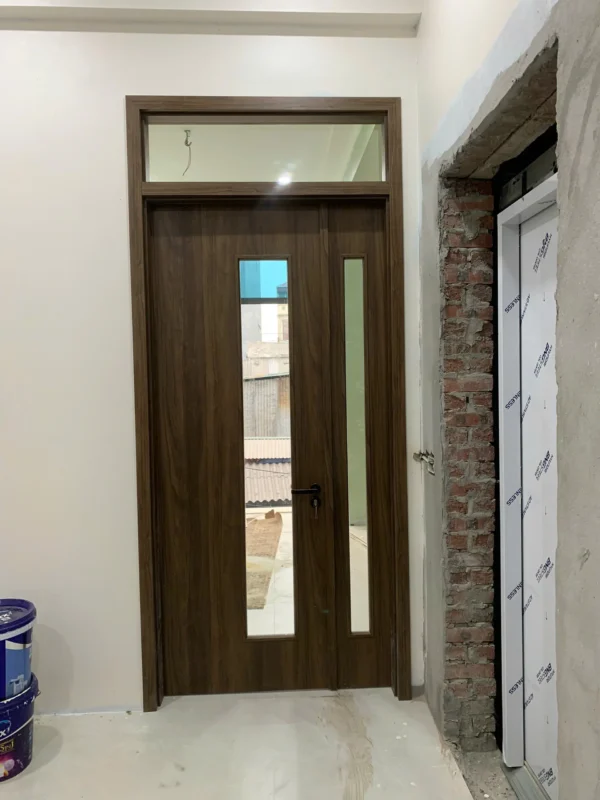 Cửa composite nâu đậm có ô kính dài, cánh phụ hẹp và ô kính cố định phía trên, tay gạt đen