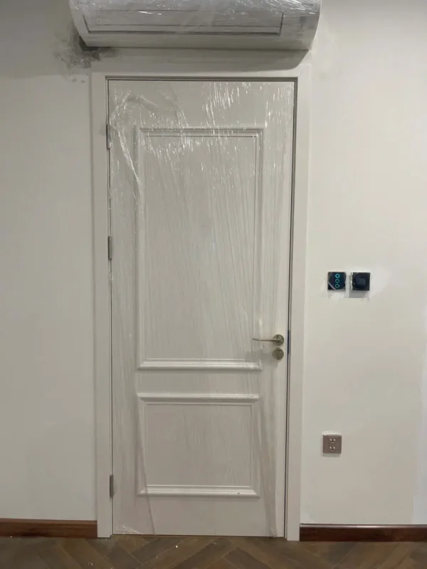 Cửa composite trắng hai ô nổi dưới máy điều hòa, sàn gỗ xương cá và công tắc cảm ứng