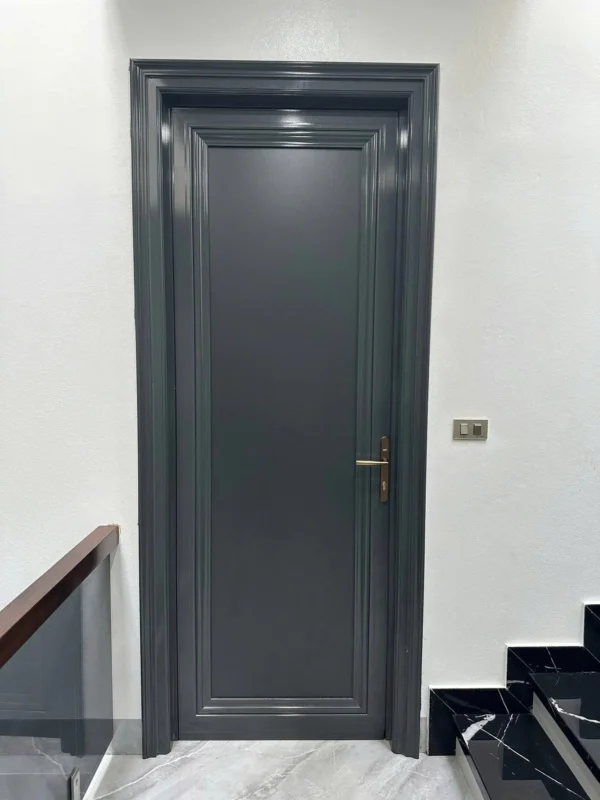 Cửa composite màu xám than khung bao chỉ dày, tay nắm màu đồng, lắp cạnh cầu thang đá đen