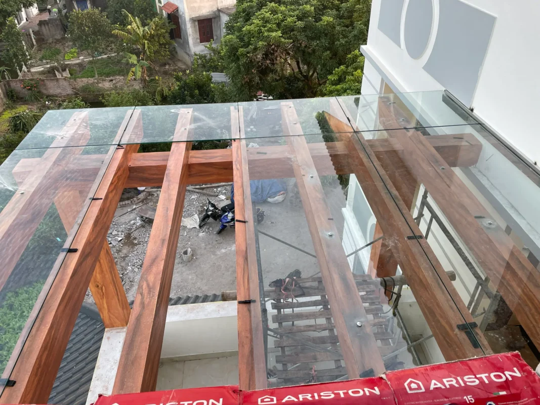 Các tấm kính trong đặt trên dầm gỗ lớn, giữ bằng bát kẹp đen và vít, chụp từ trên xuống