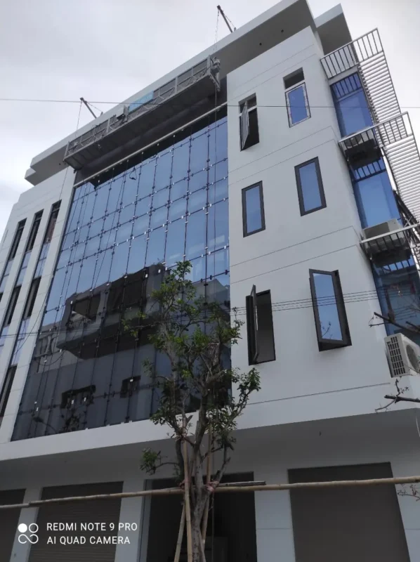 Mặt dựng kính xanh đậm lắp bằng bát kẹp ở nhà phố cao tầng, gôn nâng hạ treo ở tầng trên