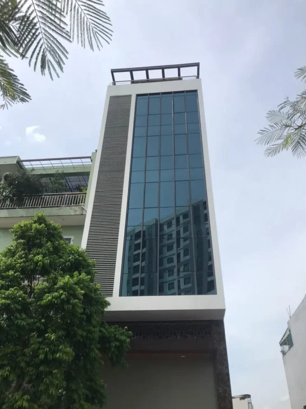 Mặt dựng kính xanh đen chạy dọc nhà phố hẹp nhiều tầng, bên cạnh là mảng lam chắn nắng