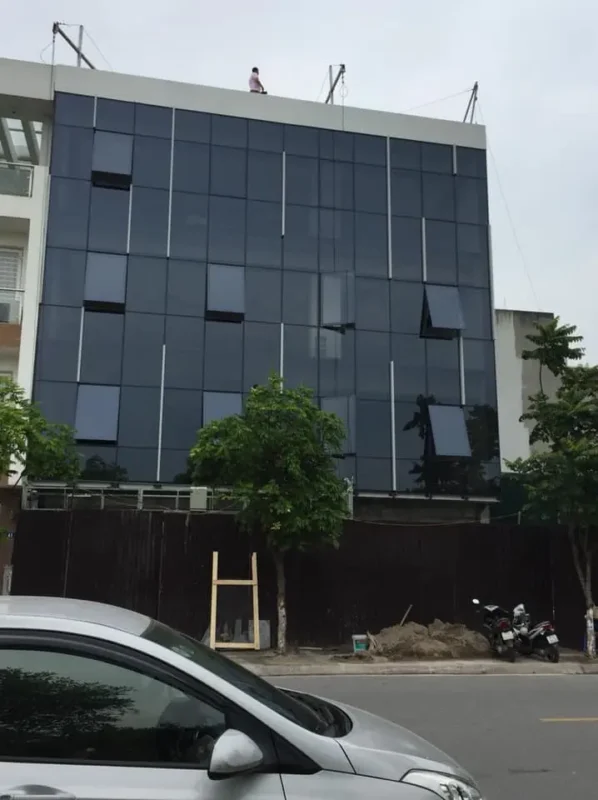 Mặt dựng kính màu xanh đen phủ kín mặt tiền nhà phố nhiều tầng, xen các ô cửa mở hất