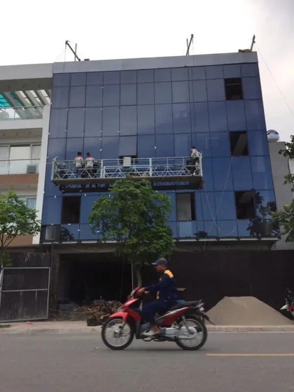 Thợ làm việc trên giàn treo để lắp vách mặt dựng kính xanh đậm cho nhà bốn tầng